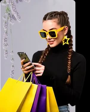 Woman with braided hair wearing yellow sunglasses and star earrings, holding colorful shopping bags while looking at her smartphone.